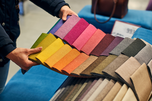 someone holds swatches of fabric over a sofa while furniture shopping