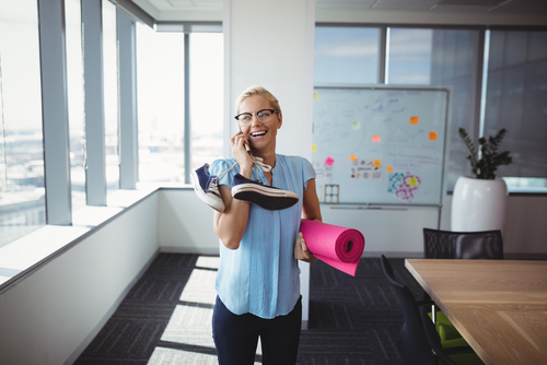 Smiling woman talks on the phone in her office while holding a yoga mat.